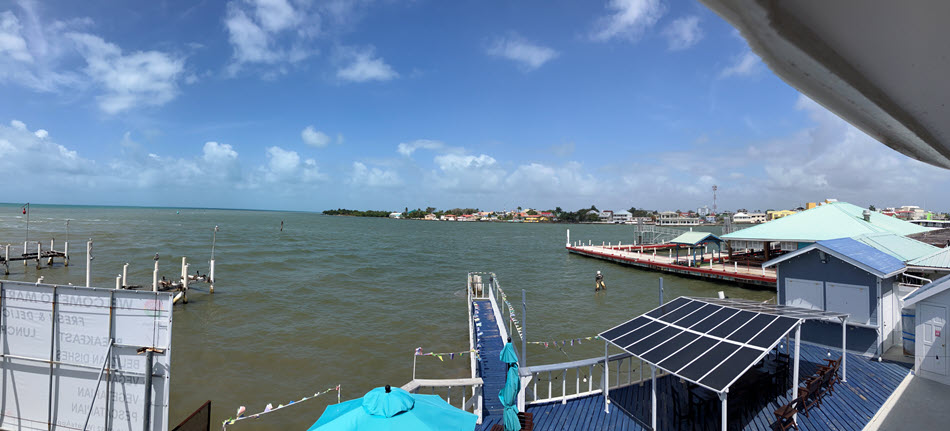 Coastal harbor view with wooden docks, blue umbrellas, and a row of houses along the shore on a sunny day