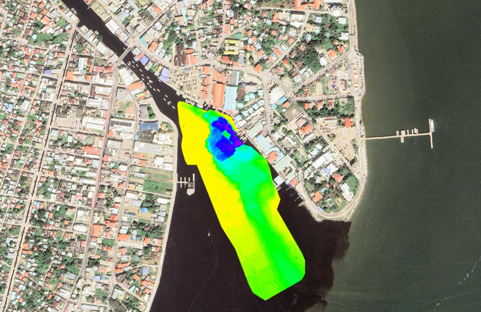 Aerial map showing a coastal town with a large yellow-green highlighted area along the water, likely representing a survey or bathymetric/impact zone overlaid on the satellite image.