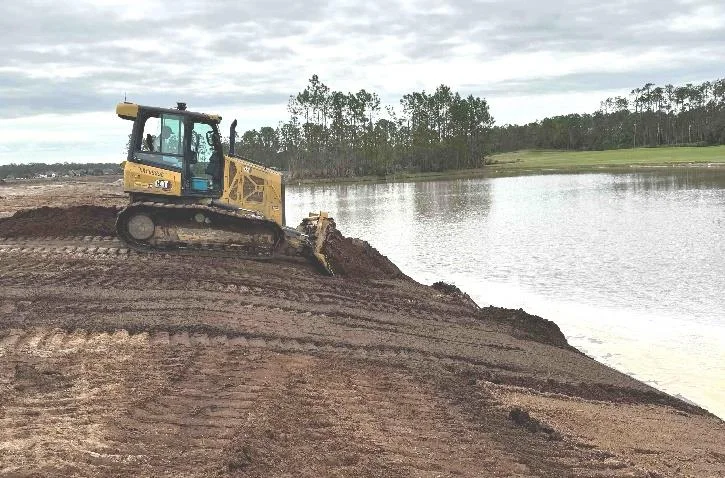 Bulldozer backfilling dirt into the construction pond