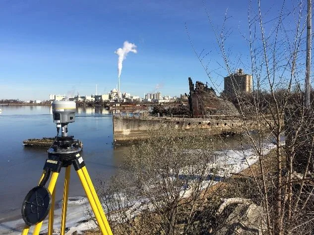 Trimble GNSS base station on a yellow tripod beside the water
