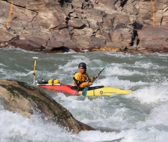 Surveyor in a kayak with a GNSS antenna working through white water rapids