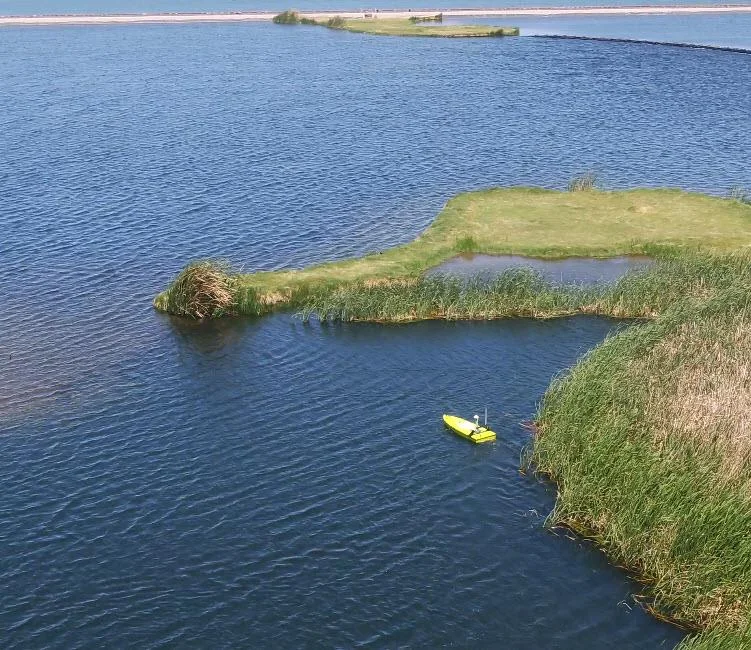 Drone view of the yellow CEE-USV on a small lagoon