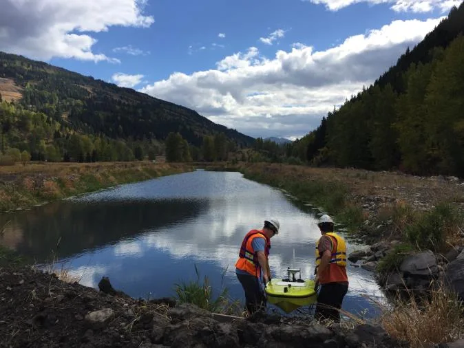 Two people in high-visibility vests deploying a CEE-USV at the edge of a coal mine pond