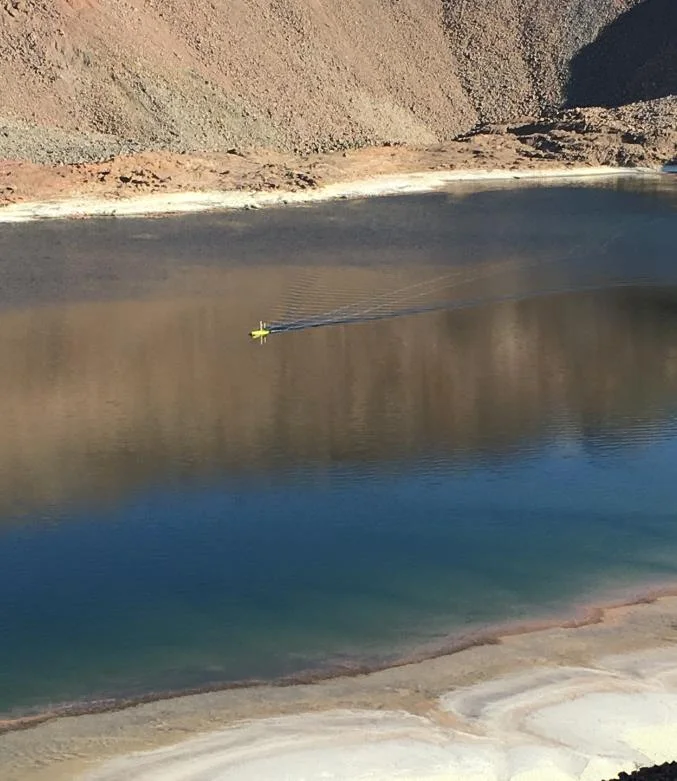 Small yellow USV surveying a blue-green pH 3 copper leachate pond