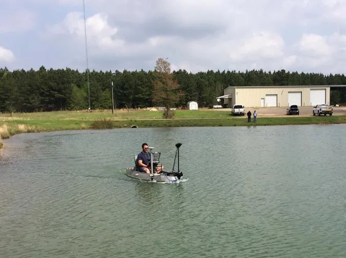 Small manned boat surveying a frac pond with buildings behind