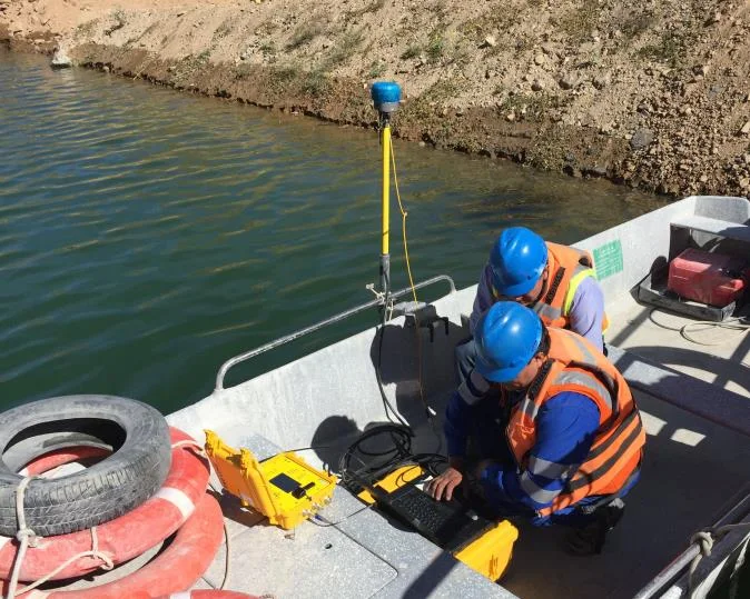 Two surveyors in hard hats on a boat with a CEE ECHO case and site RTK GNSS antenna on a pole