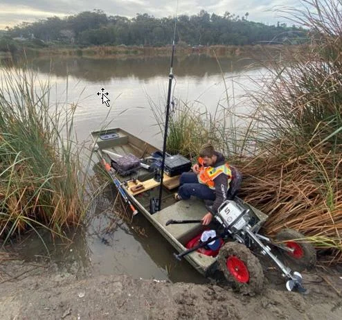 Surveyor on a small boat at the lagoon edge with the survey gear on board