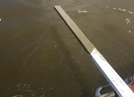 Survey pole in brown water over loosely consolidated lagoon sediment