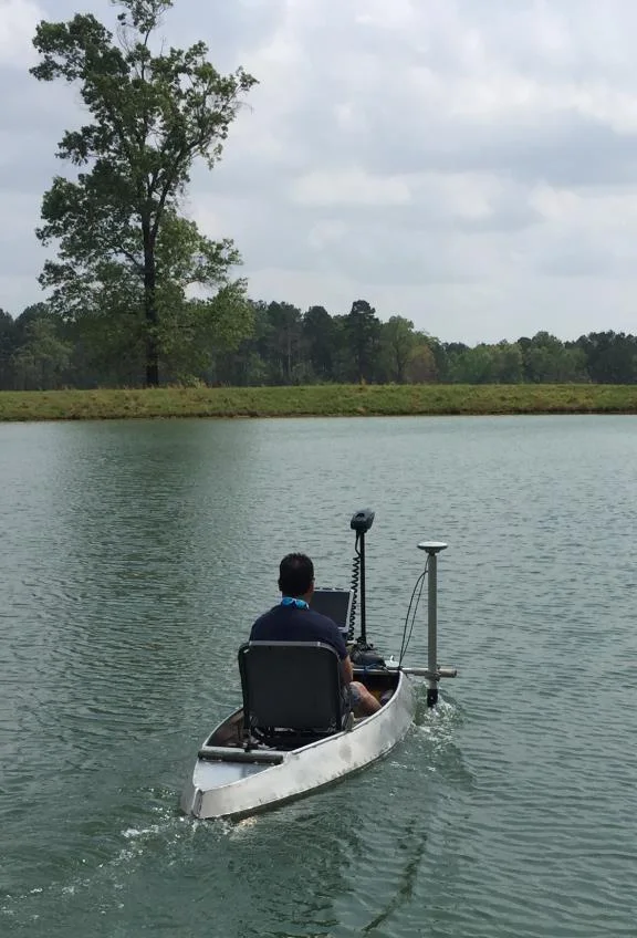 Surveyor in a small manned boat on a pond with the GPS antenna and transducer mount at the bow
