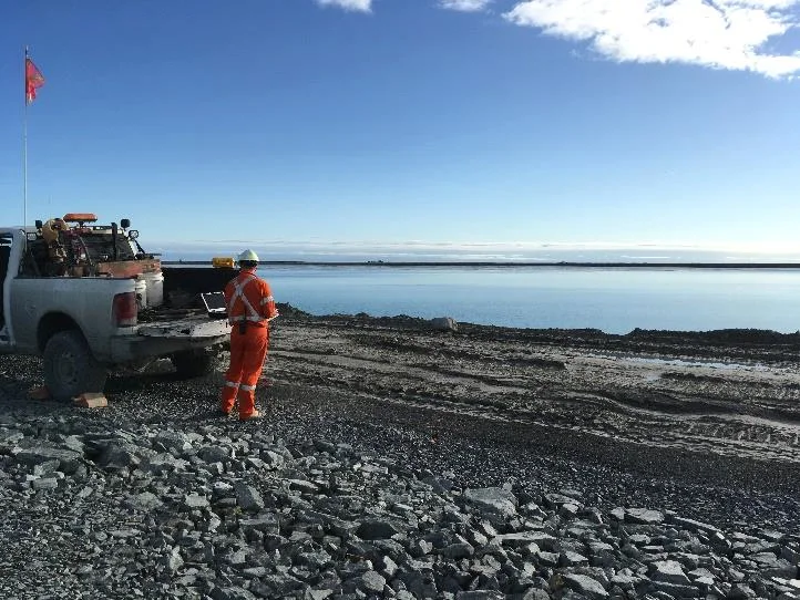 Surveyor in orange coveralls beside a pickup at the edge of a large tailings impoundment