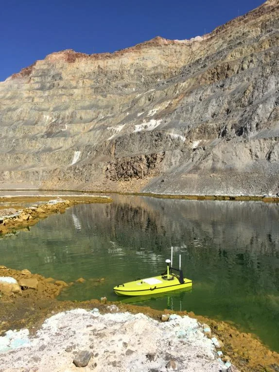 CEE-USV on green water below a layered open pit mine wall