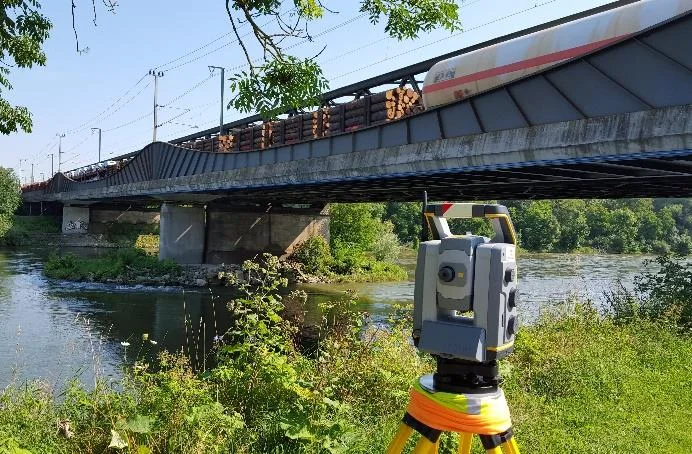 Trimble total station set up beside a river with a bridge behind