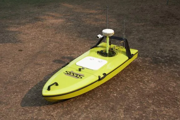 Yellow-green CEE-USV drone boat with GNSS antenna sitting on the ground