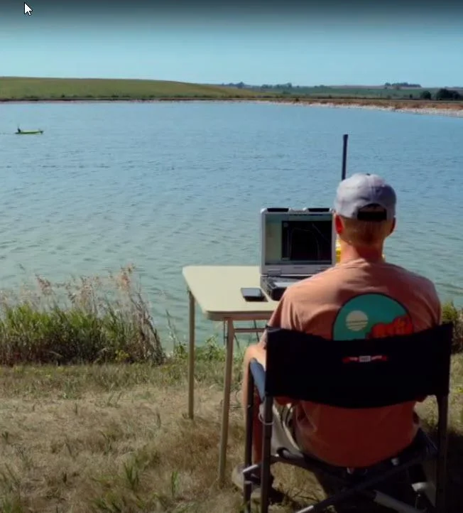 Operator at a laptop on the lagoon shore with the USV out on the water