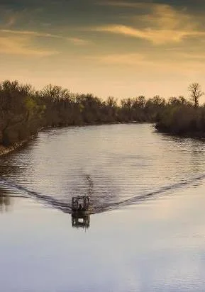 Survey boat towing the resistivity array along a river at sunset